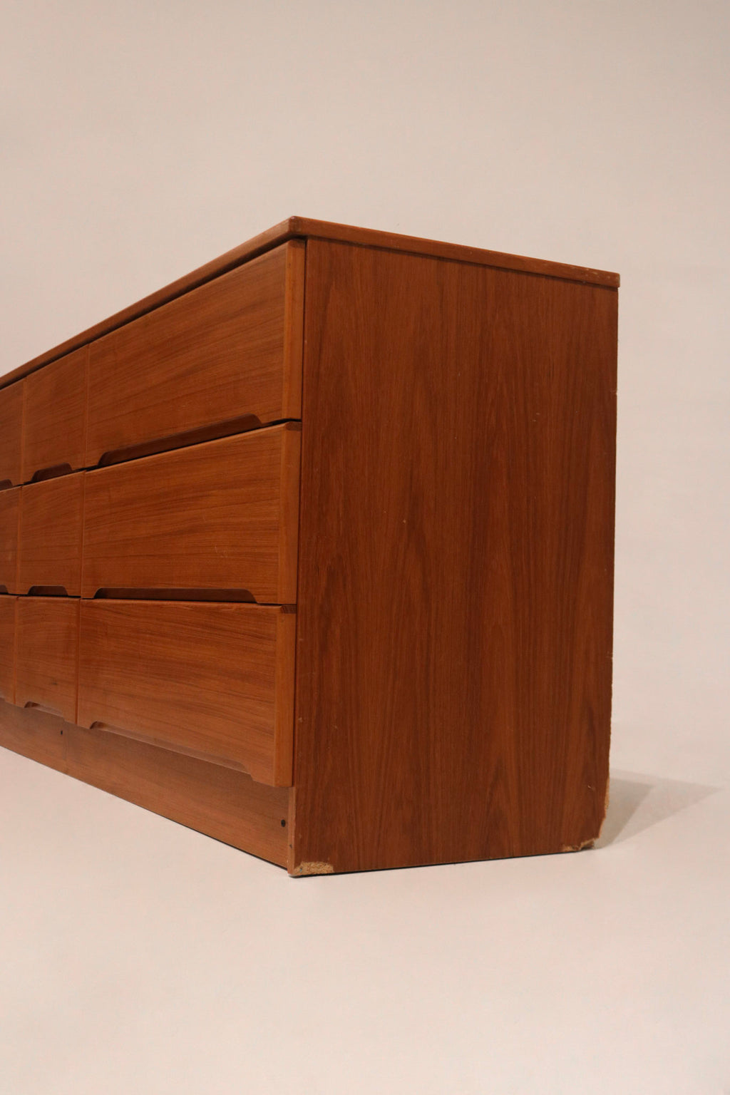 Close-up of peeling wood on bottom left side, minor cosmetic flaw on a vintage teak dresser