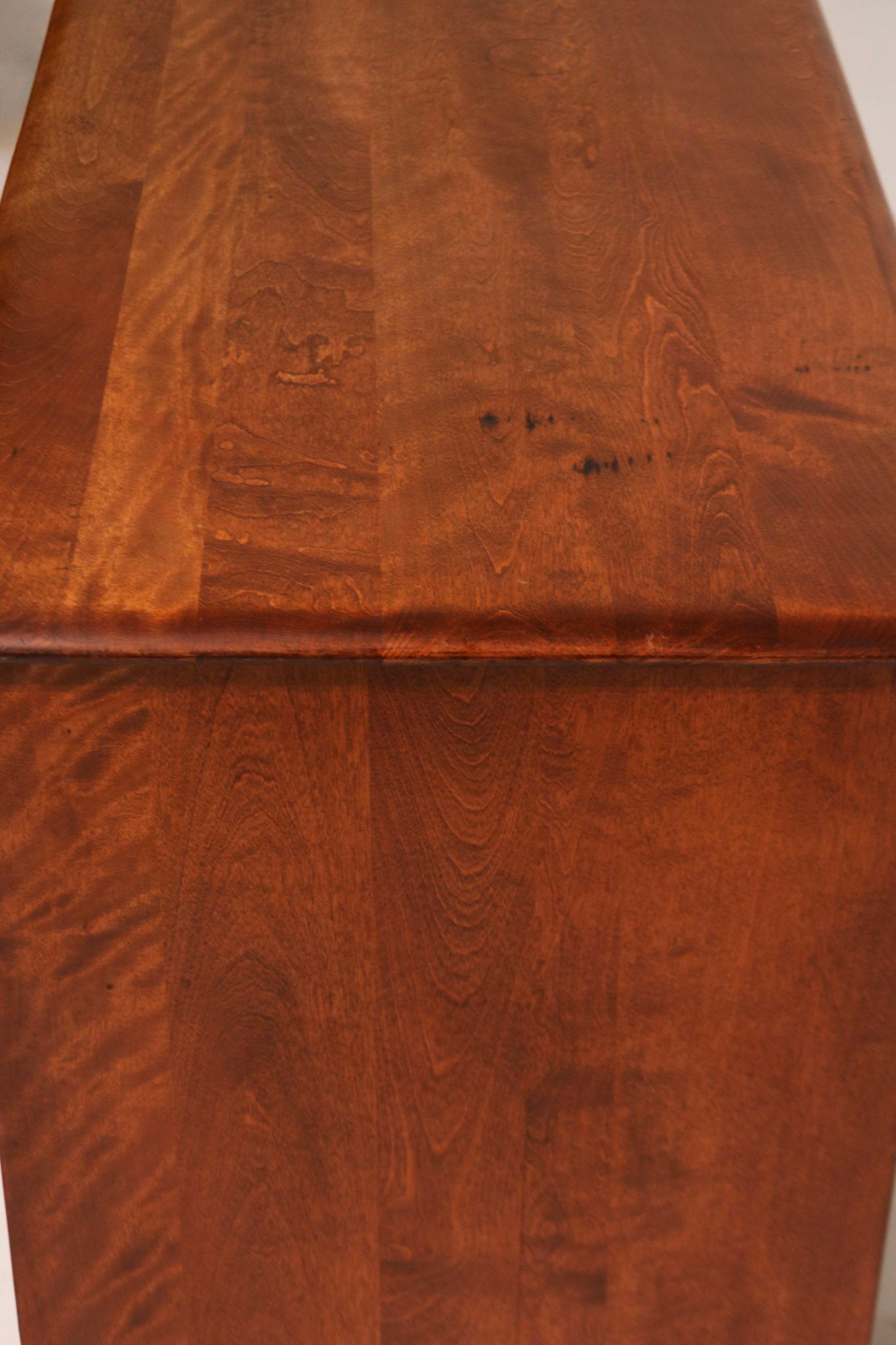 Detail of one corner leg showcasing curved design and smooth maple wood finish